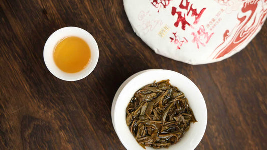 Raw pu-erh tea cake with brewed open leaves in white gaiwan and golden amber liquor on dark wood tea tray — compression brewing and aging guide